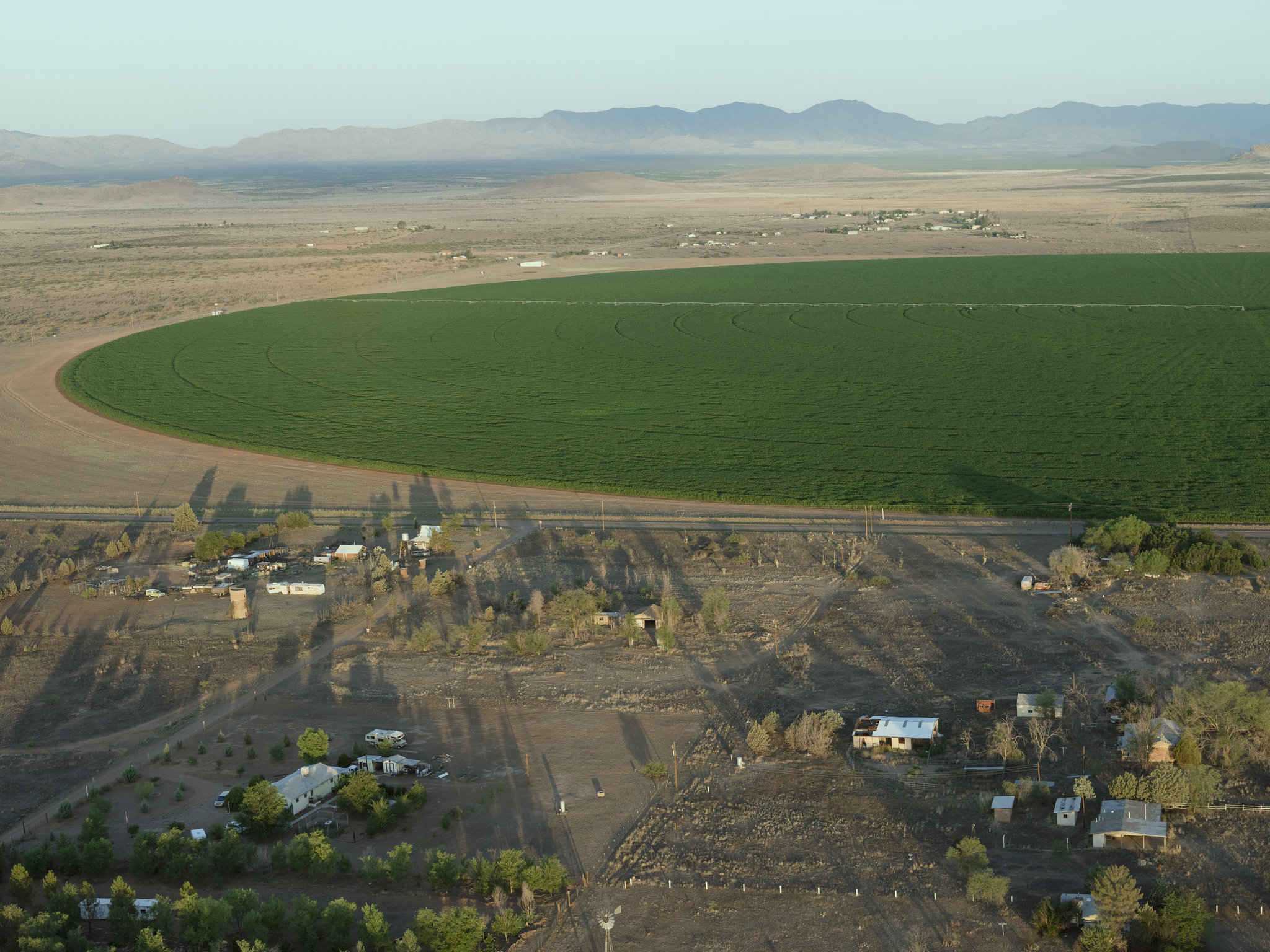 Homes in the Sulphur Springs Valley in Arizona stand just outside a corn field with a large irrigation system. (Credit: Lucas Foglia for The New York Times)